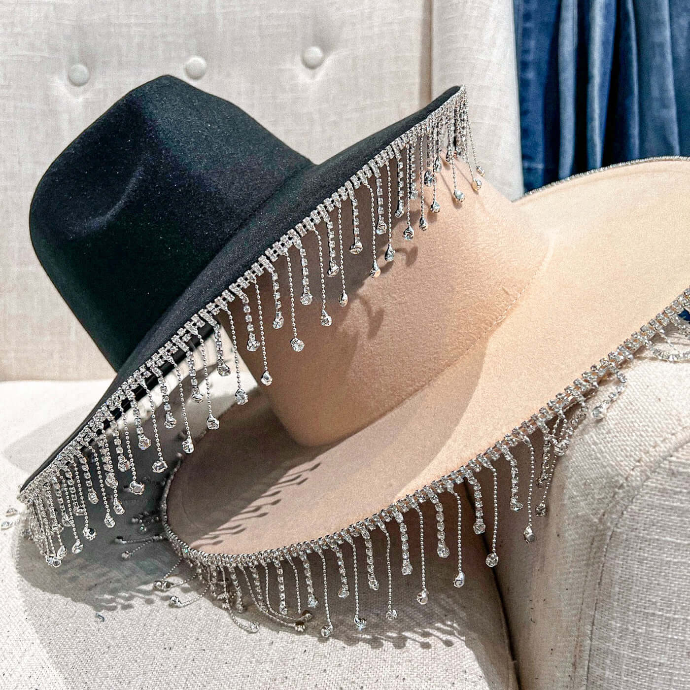 Black and cream wide brim hats with rhinestone fringe stacked on chair.