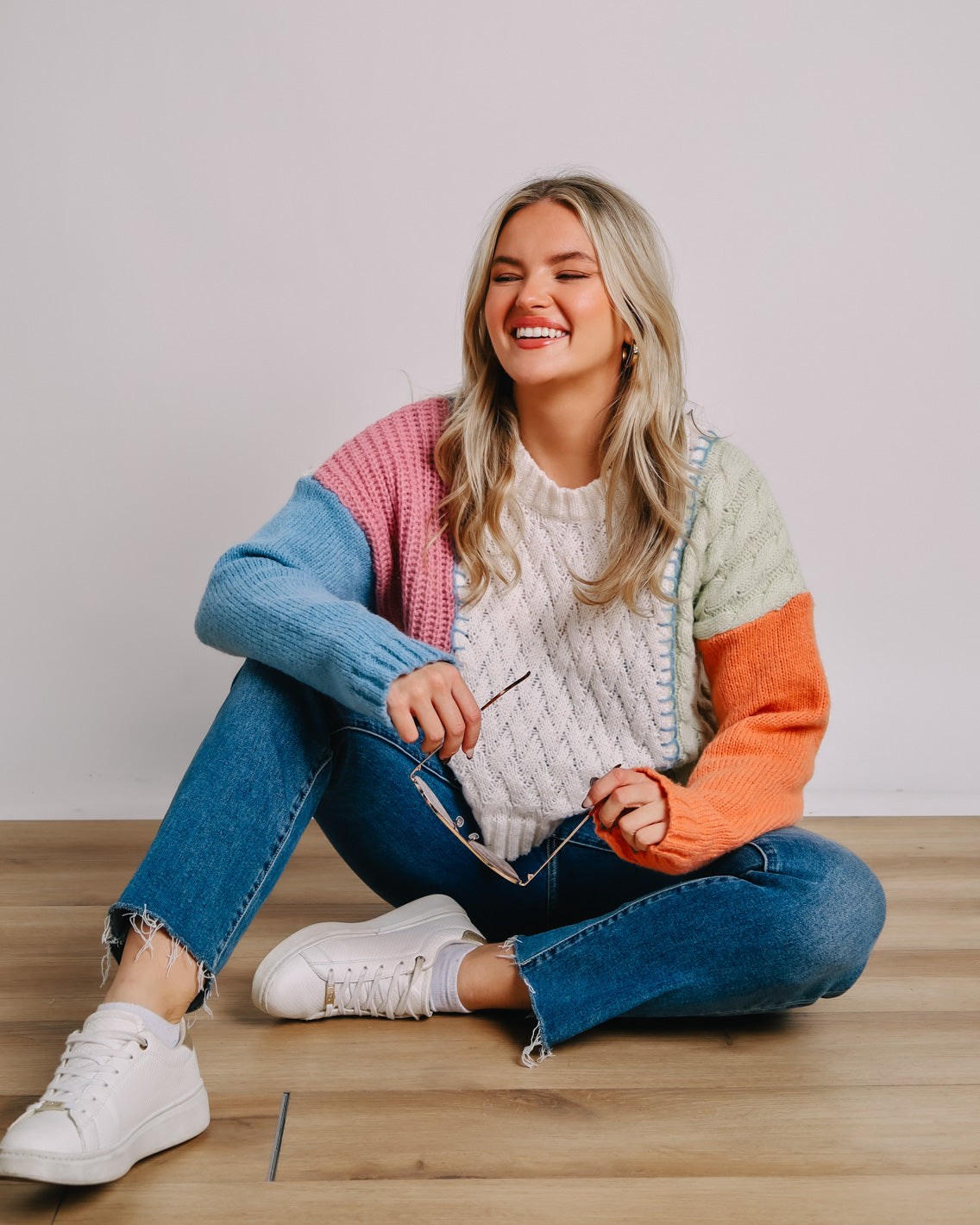 Model sitting on the ground in jeans and a colorful sweater.